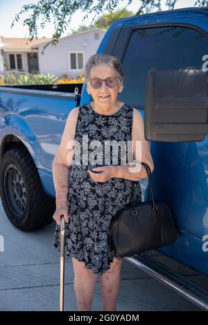 Eine 84-jährige hispanische Frau, die einen Stock in der Hand hält und neben dem Lastwagen ihres Sohnes steht. Stockfoto