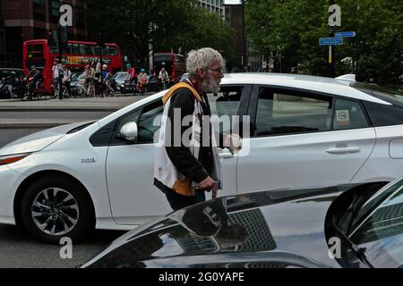 London (UK): Ein Mann mit einer Krücke geht zwischen Fahrzeugen, die an der Ampel in Elephant and Castle betteln. Stockfoto