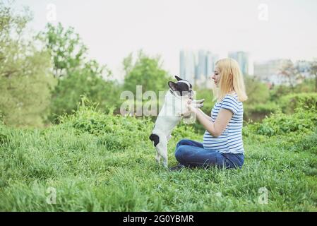 Schwangere Frau mit Hund im Grünen sonnige Natur. Gerne schwangere Frau mit ihr spielen pet im Park Stockfoto