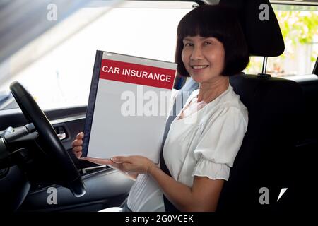 Happy Asian Senior Frau hält Kfz-Versicherung Dokument Buch und sitzen im Auto, Safety Vehicle und Schutz Client Person Konzept Stockfoto