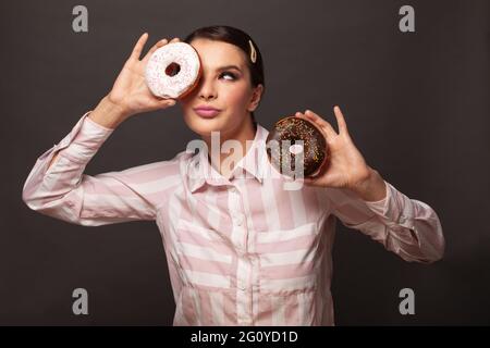 Fröhliche weibliche Modell bedeckt ihr Auge mit Donut ob schwarzen Hintergrund. Diät, Diät, Junk-Food, Schlankheits-und Gewichtsverlust Konzept Stockfoto