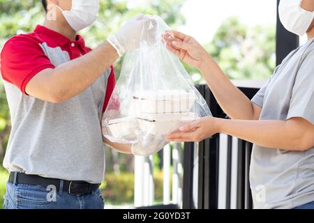 Asiatische lieferman trägt Gesichtsmaske hält Plastiktüte mit Lebensmittel-Box Lieferung an Frau Kunde Stockfoto