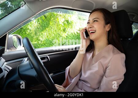 Glückliche asiatische Frau, die den Versicherungsservice anruft, während sie im Auto sitzt Stockfoto