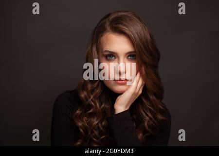 Brunette Mädchen mit langen und glänzenden welligen Haaren. Schönes Modell mit lockiger Frisur auf dunklem Hintergrund. Stockfoto