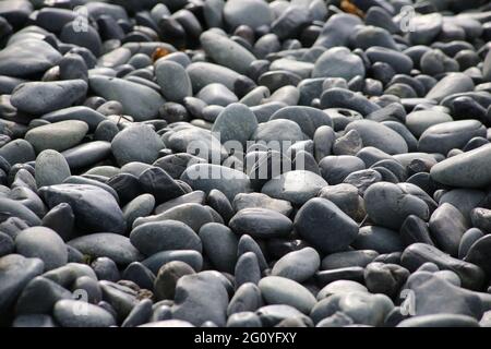 Runde Steine auf einem trockenen Flussbett draußen in der Natur. Glatte Kieselsteine mit hellgrauen Tönen bei Umgebungslicht. Stockfoto