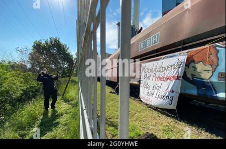 Wolfsburg, Deutschland. Juni 2021. Ein Polizeibeamter steht neben einem Kohlezug, der von Aktivisten besetzt ist, auf dem Gelände des VW-Kohlekraftwerks. Demonstranten der Aktionsgruppe "get off the Gas" besetzen seit heute früh das Kohlekraftwerk im Volkswagen-Werk in Wolfsburg. Quelle: Julian Stratenschulte/dpa/Alamy Live News Stockfoto