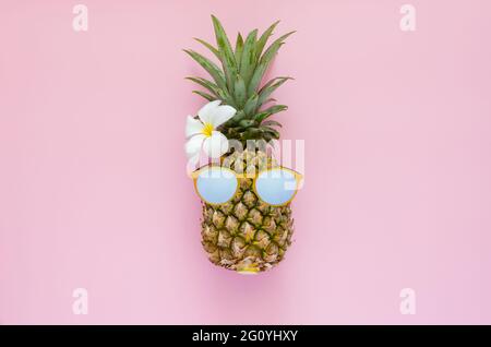 Ananas trägt Sonnenbrille mit weißer Frangipani Blume auf rosa Hintergrund. Minimales Sommerkonzept. Stockfoto