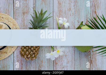Sommer-Hintergrund-Konzept mit Strandhut, Ananas, Kokosnuss, Frangipani Blumen auf blauem Holzhintergrund mit Leerraum für Text. Stockfoto