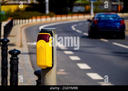 Ampeltaste an einer Fußgängerüberführung. Fußgänger-Taste auf einer Stadtstraße. Fußgängerübergangstaste mit verschwommenem Auto auf einer Straße Stockfoto