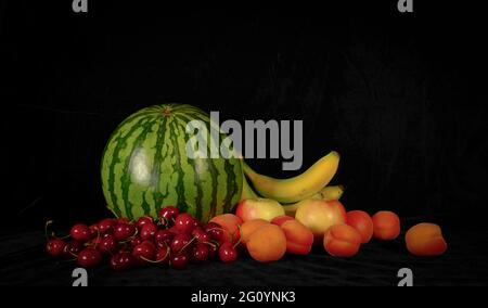 Stills von Sommerfrüchten - Wassermelone, Bananen, Kirschen und Aprikosen, auf schwarzem Hintergrund Stockfoto