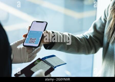 Die Fluggast zeigt einen digitalen medizinischen Pass auf ihrem Handy an die Bodenbegleiterin am Flughafen. Reisende Frau, die das Ergebnis eines digitalen covid-Schnelltests als medizinisches p Stockfoto