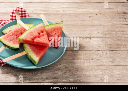 Wassermelone schneidet die Eiszapfen auf einem blauen Teller auf einem rustikalen Holztisch Stockfoto