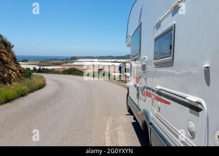 Haarnadelkurve auf einer Nebenstraße, wo sich ein Wohnmobil auf der Seite eines mit Blick in die Ferne des Meeres und Pflanzen in Gewächshäusern befindet Stockfoto