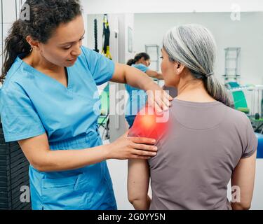 Physiotherapeutin untersucht eine Patientin mit Schultergelenkschmerzen in einer Reha-Klinik. Frau mit einer Schulterverletzung besucht ihren Chiropraktiker Stockfoto