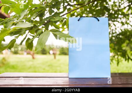 Leere Papiertüte steht auf einem Holztisch vor dem Hintergrund grüner Blätter. Stockfoto