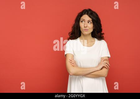 Sarkastisch zweifelhafte Frau urteilend aussehen mit skeptischem Gesicht neben leeren Kopieplatz über der roten Wand Stockfoto