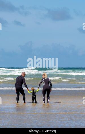 Eine Mutter und ein Vater halten die Hände mit ihrem Kleinkind, das im Meer bei Mawgan Porth in Cornwall paddelt; ein Urlaub für Familien in Cornwall. Stockfoto