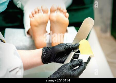 Der Pediküre-Meister, der neues Schleifpapier auf den Metallgriff aufsetzt, bevor der Fuß und die Ferse in einem Nagelstudio gereinigt werden Stockfoto