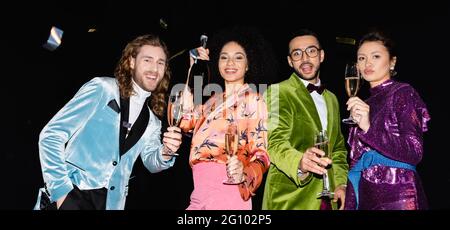 Spielerische multirassische Freunde tanzen mit Gläsern Champagner auf schwarzem Hintergrund, Banner Stockfoto