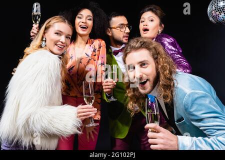 Interracial Freunde in stilvollen Kleidern trinken Champagner auf schwarzem Hintergrund Stockfoto