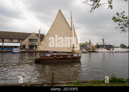 Eine Norfolk-Segelyacht, die am öffentlichen Haus des Horning Ferry Inn am Fluss Bure vorbeiführt Stockfoto