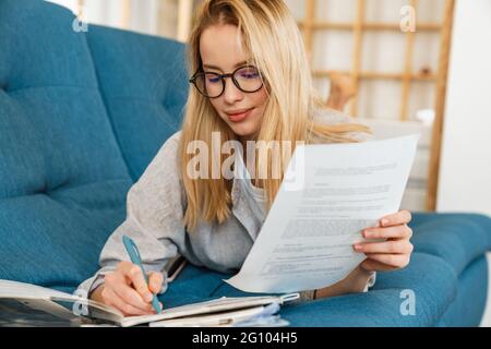 Zufrieden Student Mädchen in Brillen Hausaufgaben machen, während auf der Couch zu Hause liegen Stockfoto