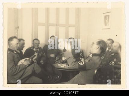 Deutsche Soldaten feiern. Eine Gruppe Wehrmachtssoldaten (Arbeitsdienst) feiert und singt. Einer von ihnen spielt auf einer Mandoline. Trinken Sie und eine Kerze in einer Flasche. An der Wand ein Porträt von A. Hitler. Stockfoto