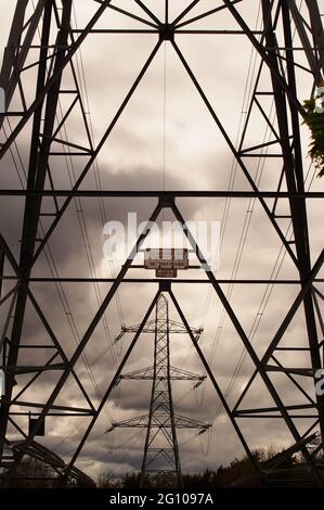 Ein Blick durch einen Strompylon, Übertragungsturm, auf einen anderen Strompylon, der Symmetrie mit einem trüben grauen Himmel zeigt Stockfoto