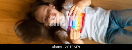 Anti Stress sensorische Pop es Spielzeug in den Händen eines Kindes. Ein kleines glückliches Mädchen spielt mit einem einfachen Grübchen Spielzeug zu Hause. Kleinkind hält und Pop spielen Stockfoto