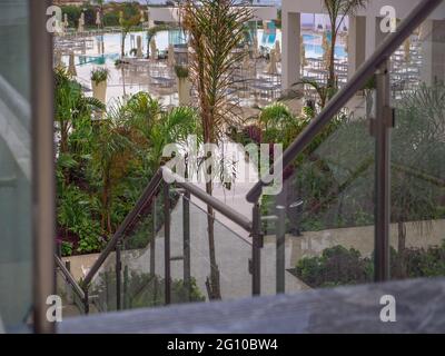 Blick unten auf einen Hotelhof mit Swimmingpool, Sonnenliegen, Sonnenschirmen und Grün an einem üblen Regentag in Napa, Zypern. Einsames Hotel. Stockfoto