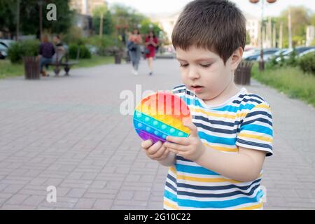 Ein Kind von 4 Jahren spielt mit Pop IT im Stadtpark. Anti-Stress-Spielzeug für die Entwicklung von Feinmotorik bei Kindern. Stockfoto