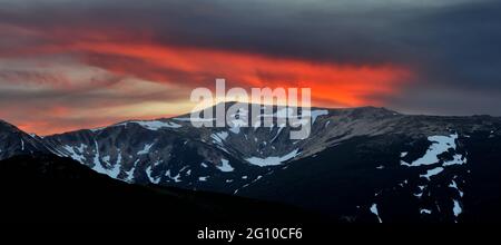 Dramatischer Sonnenuntergang in den Bergen. Viwid rot und blau Himmel mit riesigen Wolke und Berge Silhouetten mit schmelzendem Schnee bedeckt. Karpaten, Großbritannien Stockfoto