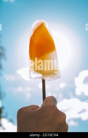 Gefrorene Eiszapfen auf Stock in der Hand des Kindes auf dem Hintergrund des blauen Himmels. Eis mit Orangen- und Zitronenscheiben. Vertikal Stockfoto