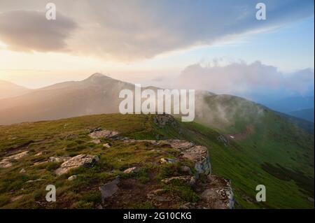 Dramatischer Sonnenuntergang in den Bergen. Leichter Nebel, der durch den Grat fließt und starke Regenwolken. Stockfoto