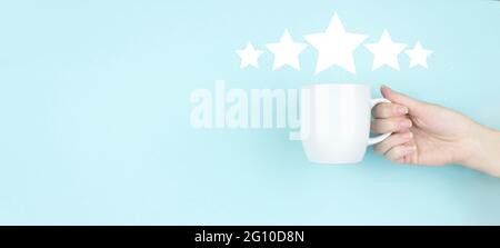 Customer Experience Konzept. Mädchen Hand halten Morgen Kaffeetasse mit fünf Sternen 5 Rating-Zeichen-Symbol auf blauem Hintergrund. Bewertungsbewertung erhöhen und c Stockfoto