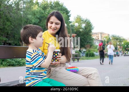 Mama und kleiner Sohn trinken im Park in der Stadt Kakao. Kakao oder Milchshake im Sommer im Freien, Familienurlaub. Stockfoto