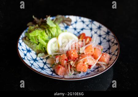 Würziger Lachs-Sashimi-Salat mit Gemüse auf Keramikplatte im japanischen Restaurant Stockfoto