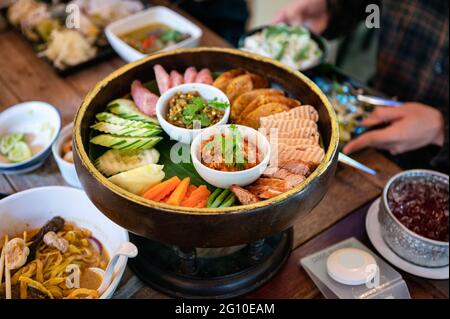 Stellen Sie eine Vorspeise aus Northern Thai Food mit gebratenem Schweinefleisch, Wurst, Gemüse und thailändischer Chilisauce auf Khantoke oder einem traditionellen Behälter im Restaurant ein Stockfoto