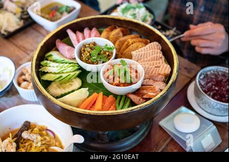 Stellen Sie eine Vorspeise aus Northern Thai Food mit gebratenem Schweinefleisch, Wurst, Gemüse und thailändischer Chilisauce auf Khantoke oder einem traditionellen Behälter im Restaurant ein Stockfoto