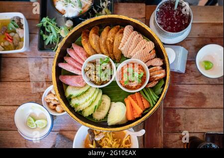 Stellen Sie eine Vorspeise aus Northern Thai Food mit gebratenem Schweinefleisch, Wurst, Gemüse und thailändischer Chilisauce auf Khantoke oder einem traditionellen Behälter im Restaurant ein Stockfoto