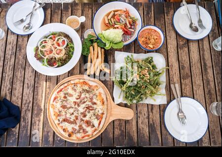 Vielfalt an Speisen mit Pizzafleisch, Käse, knusprigem Gemüse, würzigem Salat und Geschirr auf Holztisch im Restaurant Stockfoto