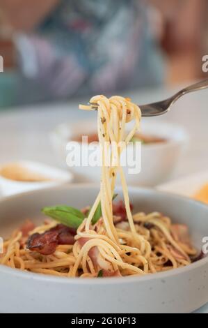 Hand halten Chilli Speck Grill Spaghetti Rolle mit Gabel auf Keramikplatte im Restaurant Stockfoto