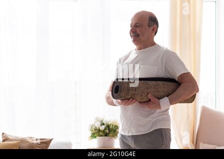 Ein älterer Mann mit einer Yogamatte blickt lächelnd auf die Kamera Stockfoto