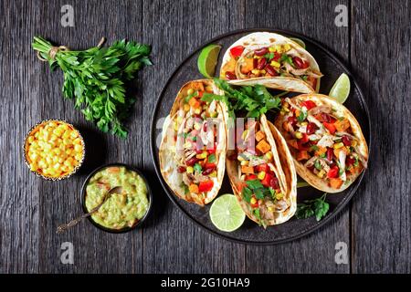 Tacos aus Mehl Tortilla Schalen Füllung mit gegrilltem Hühnerfleisch, Mais, gerösteten Süßkartoffeln Würfel, rotem Pfeffer und Petersilie auf einem schwarzen Teller serviert Stockfoto