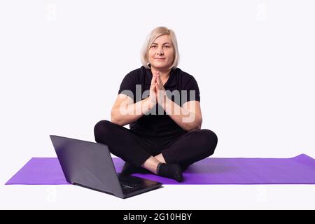 Ältere Sportlerin, fit sportlich gesunde Frau sitzen in Yoga-Pose auf der Matte, machen Atemübungen, beobachten Online-Yoga-Kurs auf Laptop-Computer Stockfoto