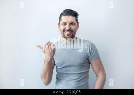 Hübscher Hipster lächelnder Mann zeigt mit Erstaunen weg, während er neues Angebot zeigt. Seht dort hin! Achtung weg, zeigt mit dem Daumen. Stockfoto