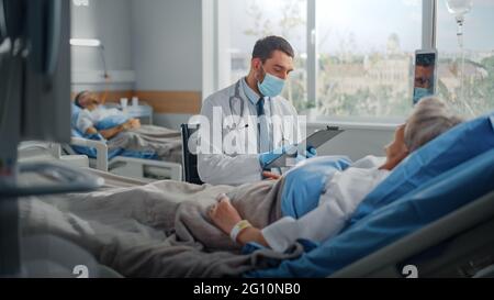 Krankenhausabteilung: Freundlicher Arzt mit Gesichtsmaske spricht mit einer schönen älteren Patientin, die im Bett ruht, erklärt die Testergebnisse und gibt Ratschläge zur Genesung Stockfoto