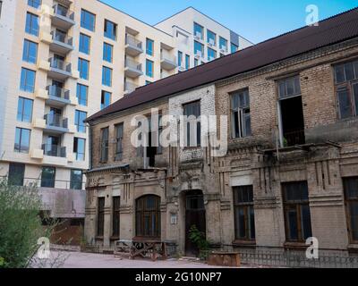 Das Äußere eines alten, halb ruinierten zweistöckigen, verlassenen Backsteingebäudes im Schatten eines neuen, frisch erbauten Hochhauses im Zentrum von Kiew, Ukraine. Stockfoto