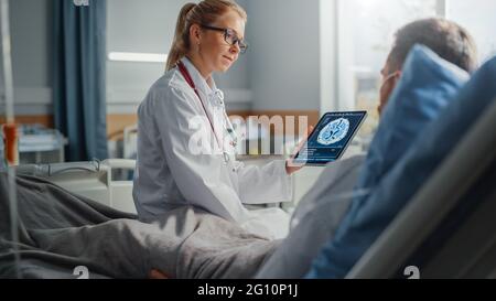 Krankenhausabteilung: Freundliche Ärztin spricht mit kranken männlichen Patienten, die sich im Bett ausruhen, verwendet einen Tablet-Computer, zeigt und erklärt die Ergebnisse von Gehirnscans Stockfoto
