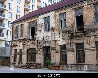 Das Äußere eines alten, halb ruinierten zweistöckigen, verlassenen Backsteingebäudes im Schatten eines neuen, frisch erbauten Hochhauses im Zentrum von Kiew, Ukraine. Stockfoto